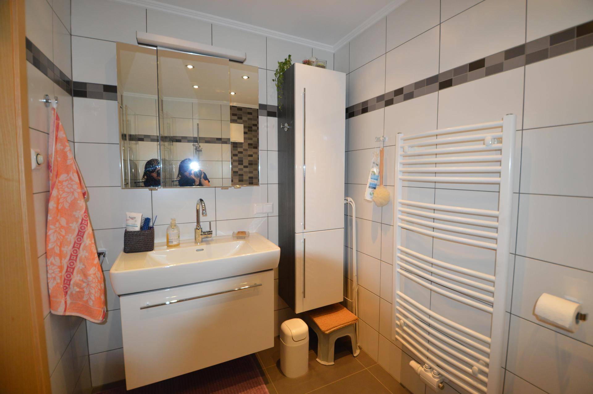 Modernes Badezimmer mit weißen und grauen Fliesen, Einzelwaschbecken und Handtuchheizkörper.
