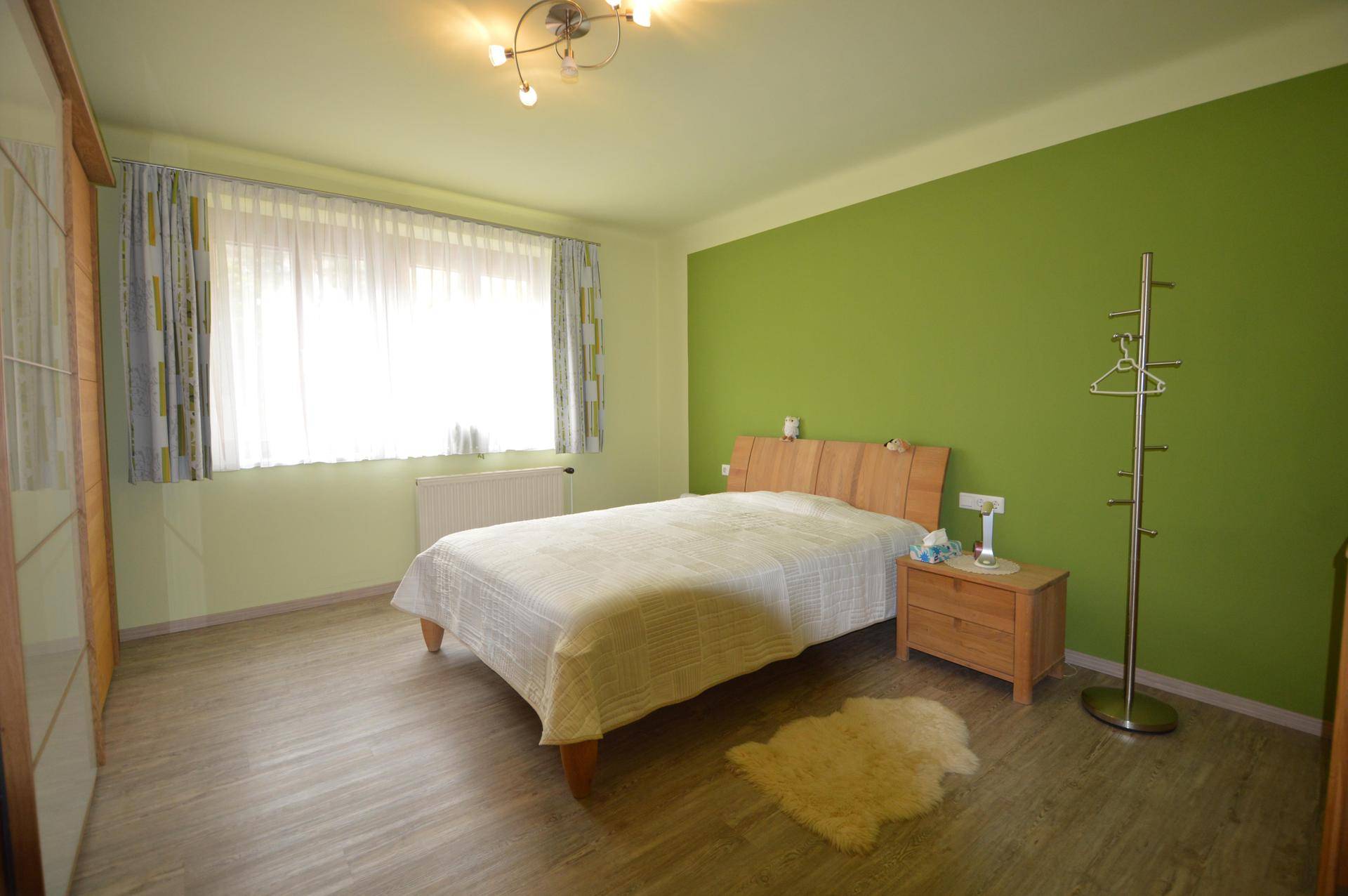 Schlafzimmer mit Holzbett, grüner Akzentwand und modernem Laminatboden.