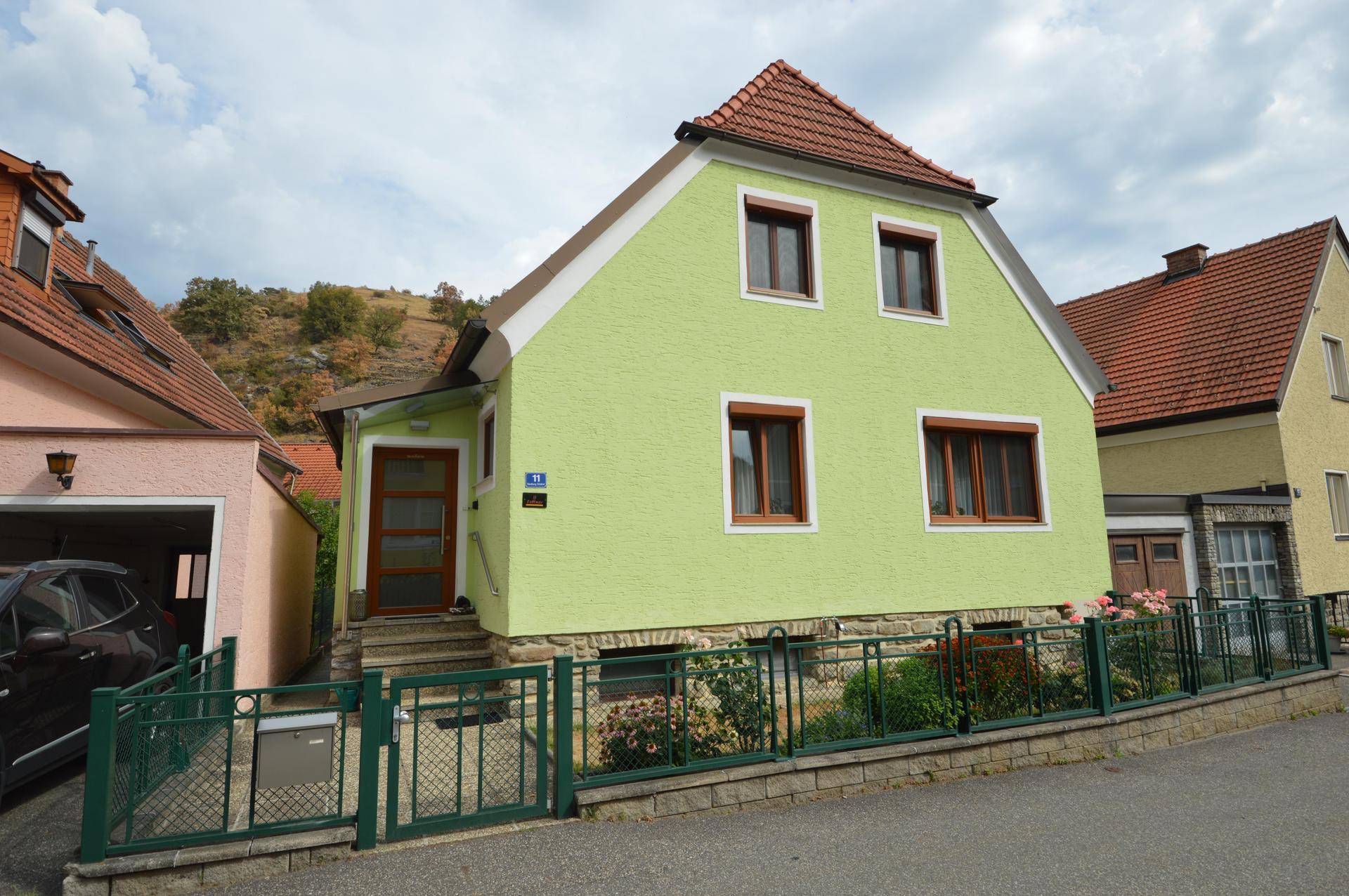 Vorderansicht des hellgrünen Hauses von der Straße aus mit kleinem Vorgarten und Garage.