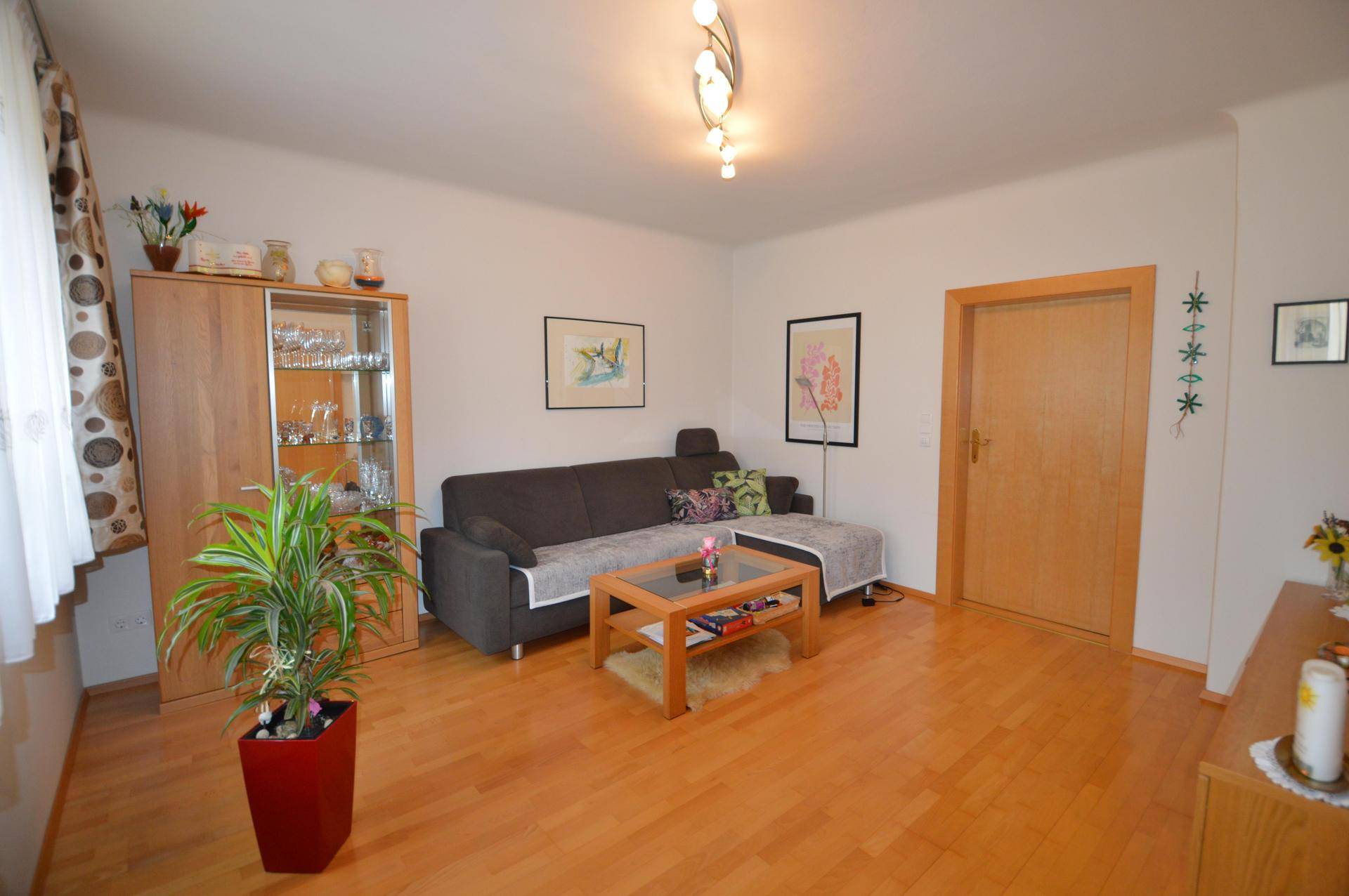 Helles Wohnzimmer mit dunklem Sofa, Holzmöbeln und hellem Laminatboden.