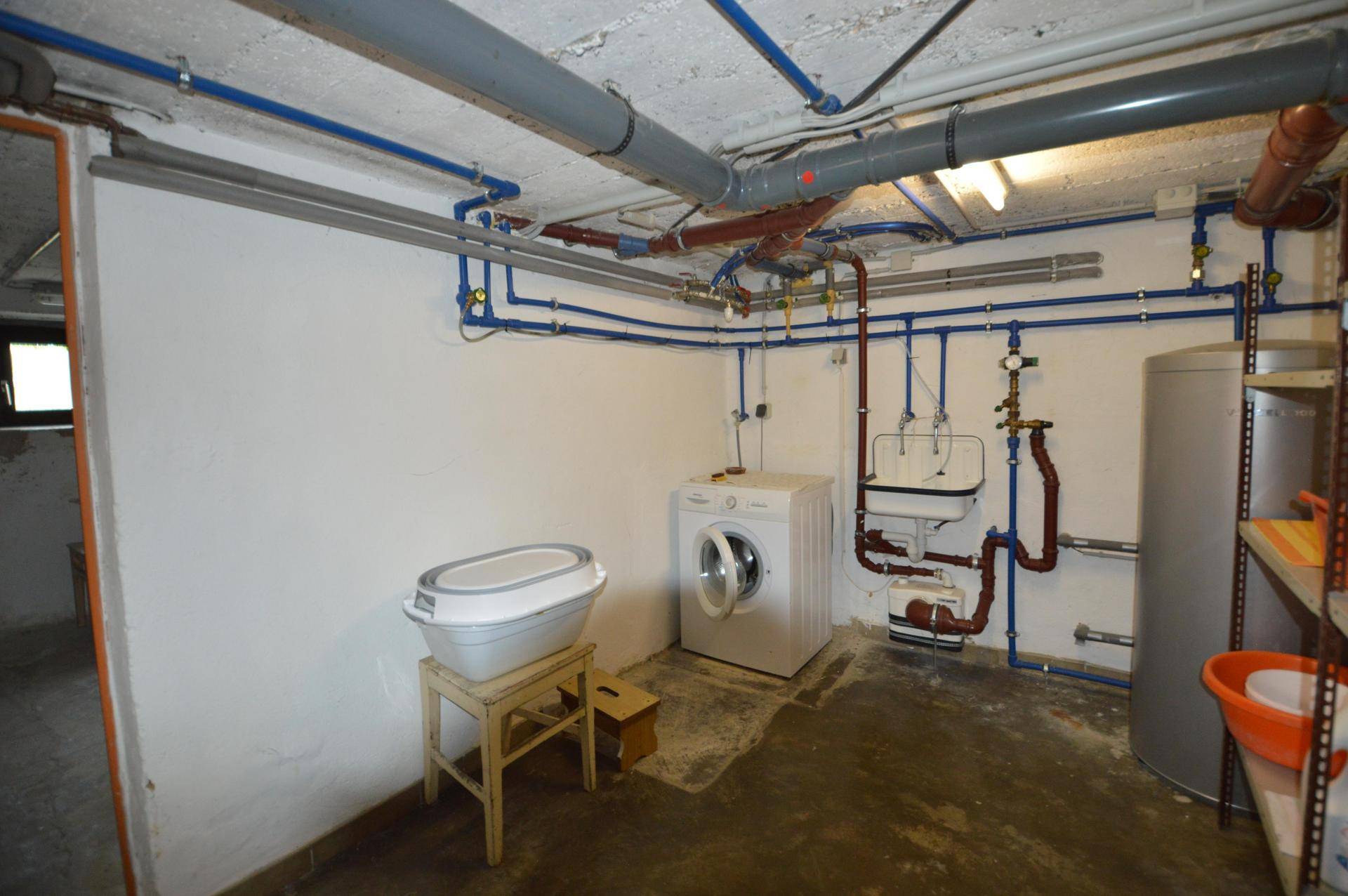 Kellerraum mit sichtbaren Leitungen, Waschmaschine und Warmwasserbereiter.