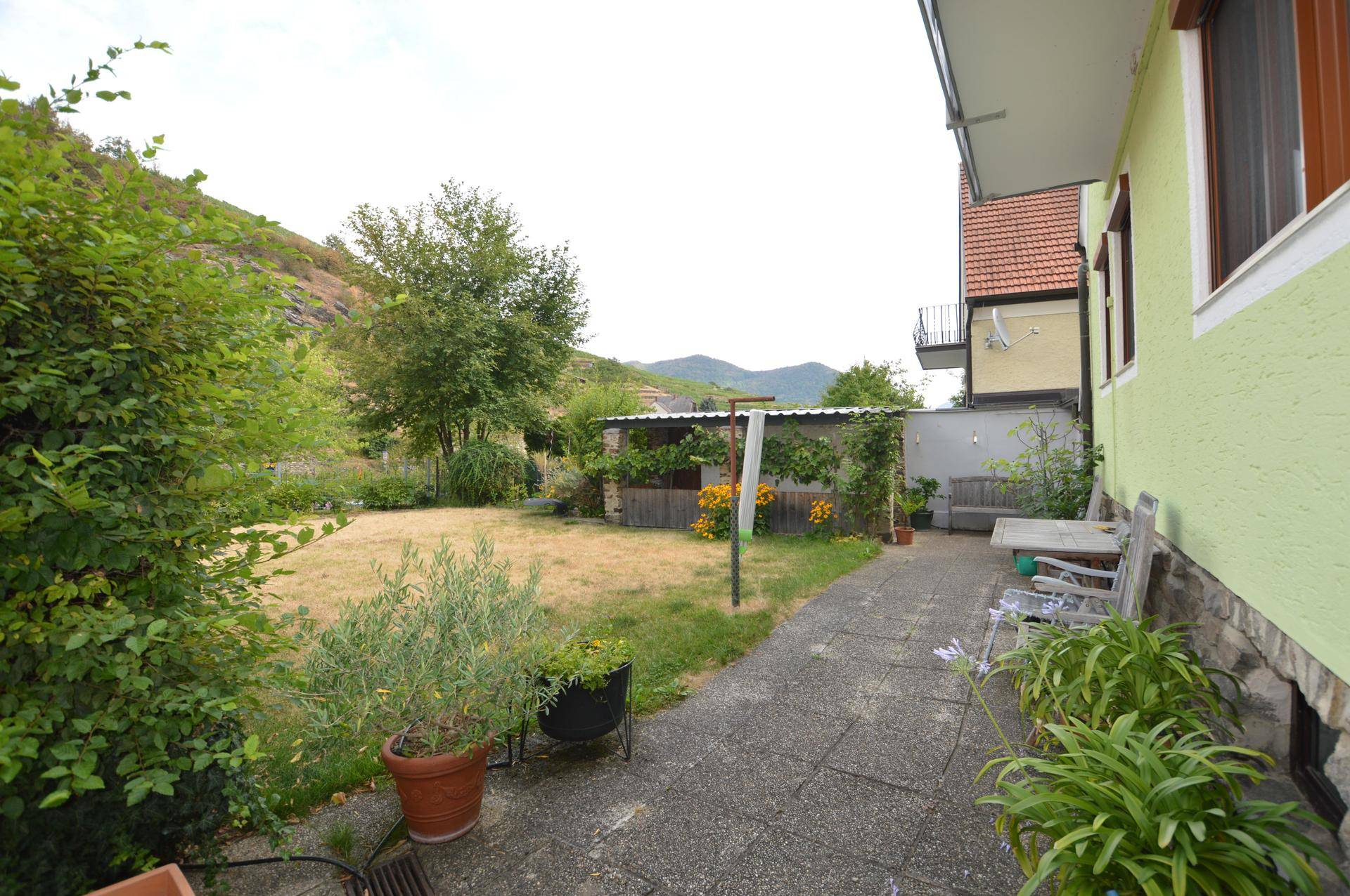 Gartenbereich mit gepflasterter Terrasse, Sitzgelegenheiten und Blick auf die Hügellandschaft.