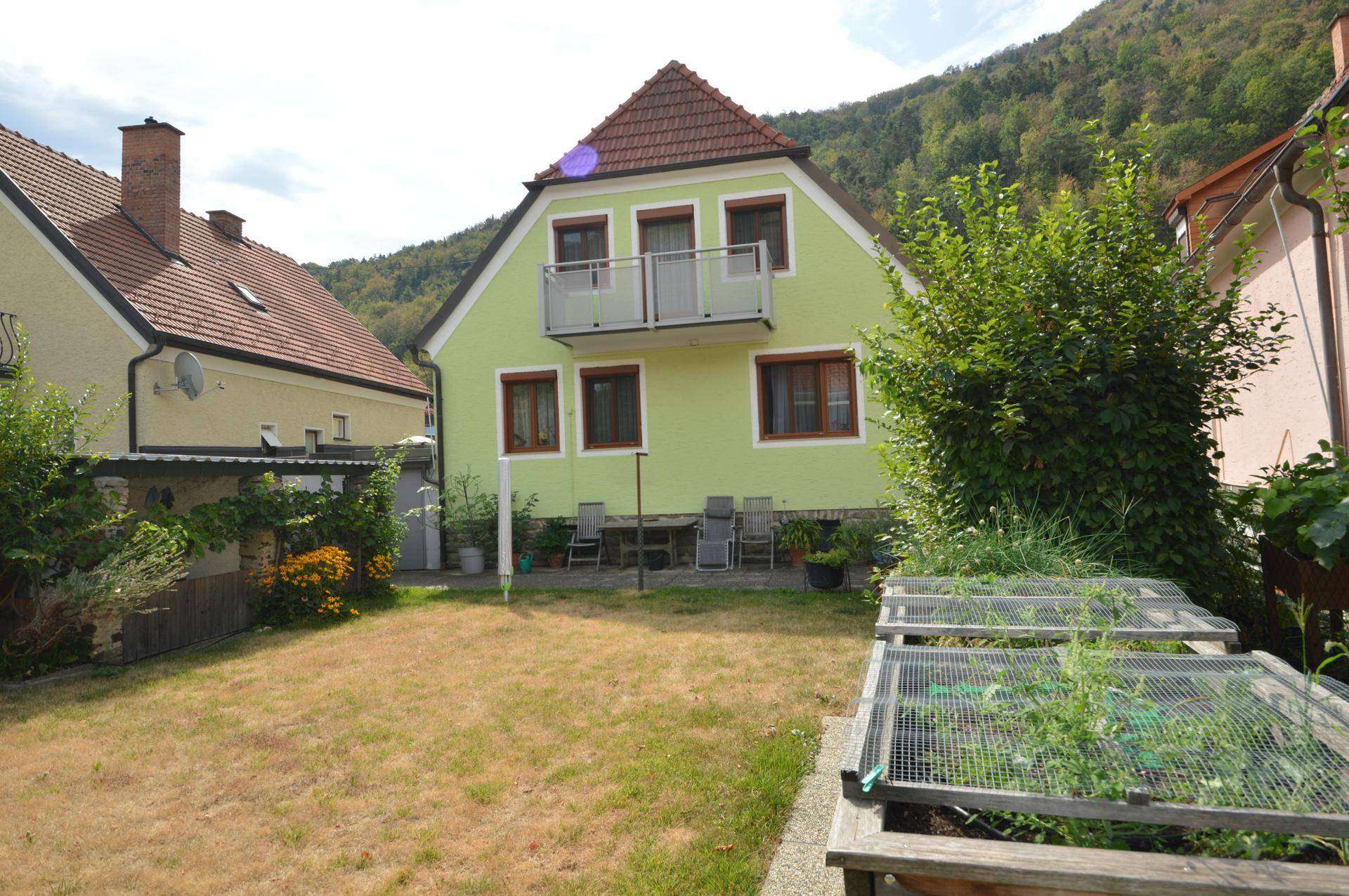 Hinteransicht des Hauses mit Garten, Balkon und Hochbeeten für den Anbau.