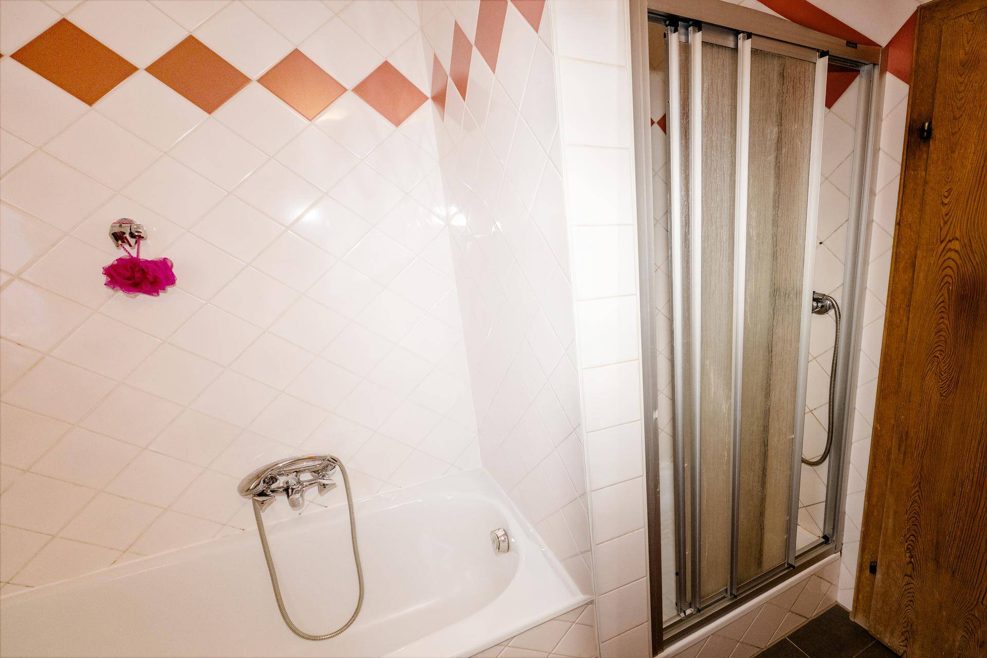 Badezimmer mit Badewanne und Duschkabine, ausgestattet mit weißen Fliesen und orangefarbenen Akzenten.