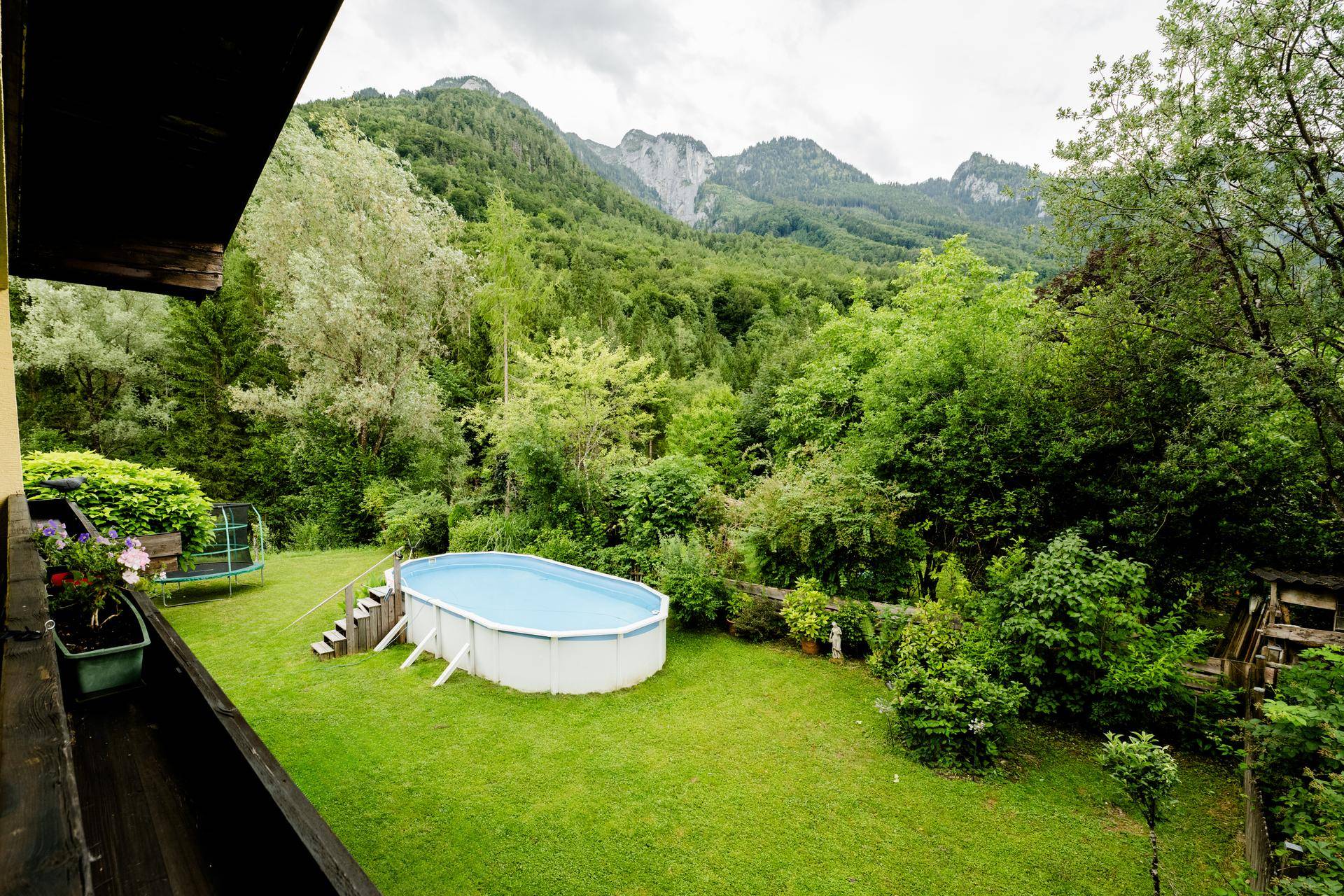 Blick vom Balkon auf den Garten mit Pool, Trampolin und der beeindruckenden Berglandschaft im Hintergrund.