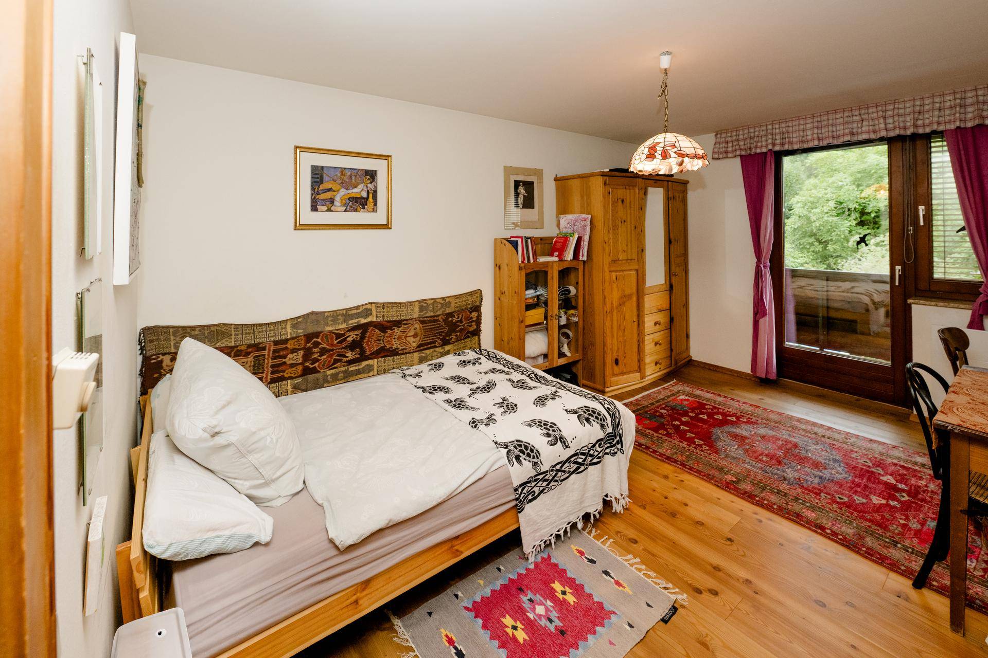 Helles Schlafzimmer mit Einzelbett, Holzmöbeln und Zugang zu einem Außenbereich.