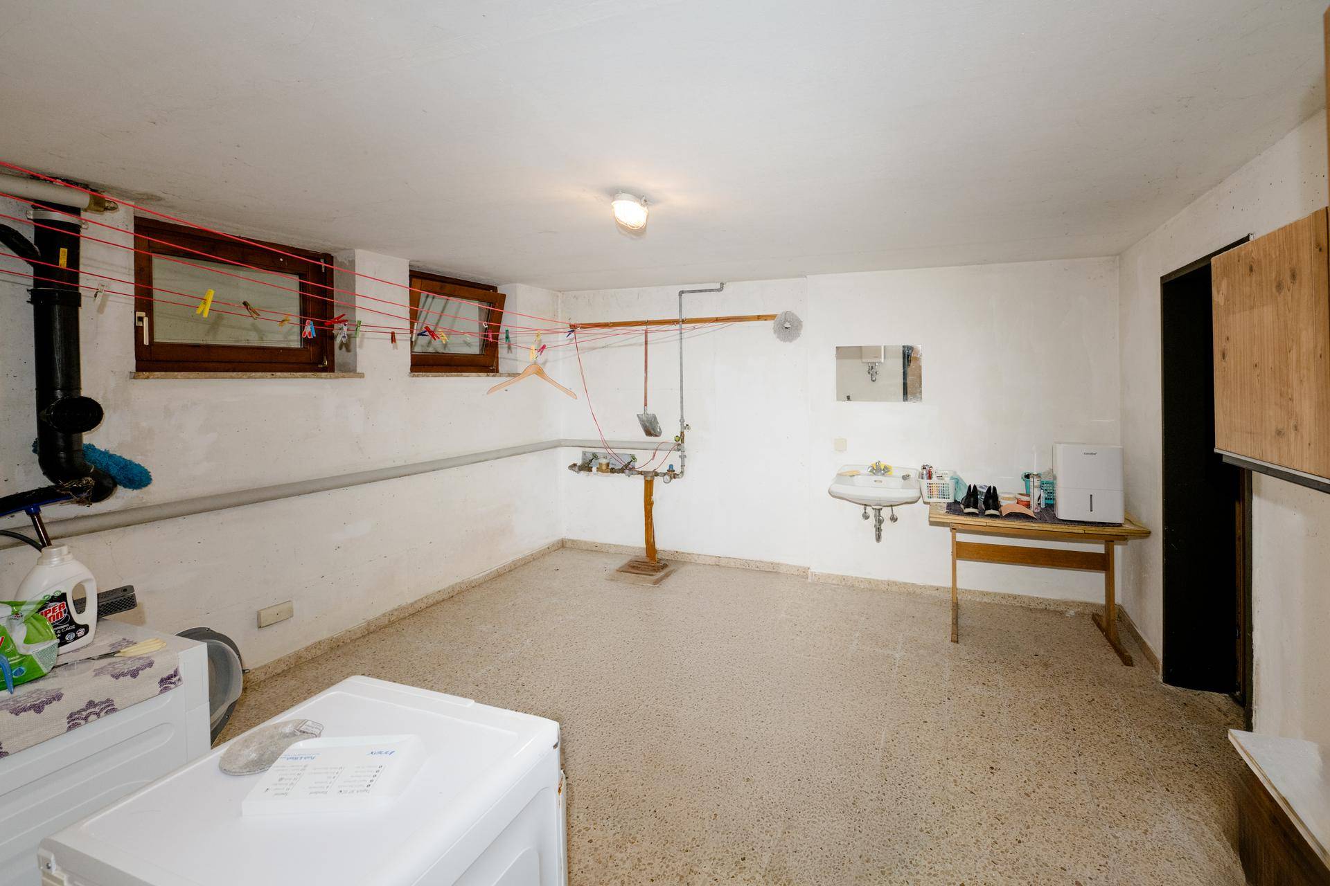 Praktischer Waschraum im Keller mit Waschmaschine, Waschbecken und Wäscheleinen.
