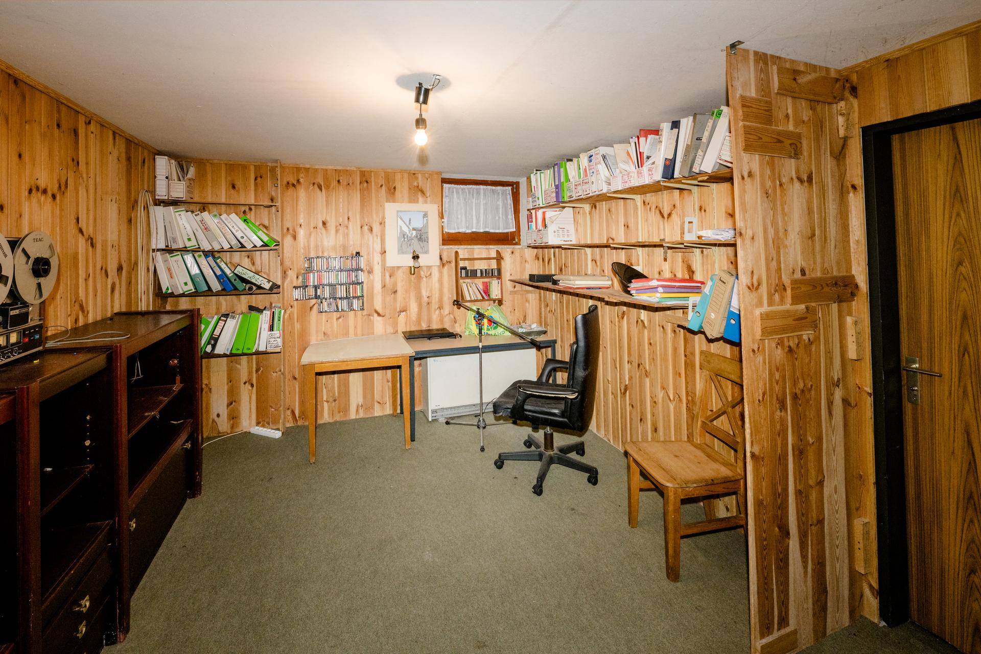 Kellerraum mit Holzvertäfelung, Regalen und Teppichboden, ideal als Hobby- oder Arbeitszimmer.