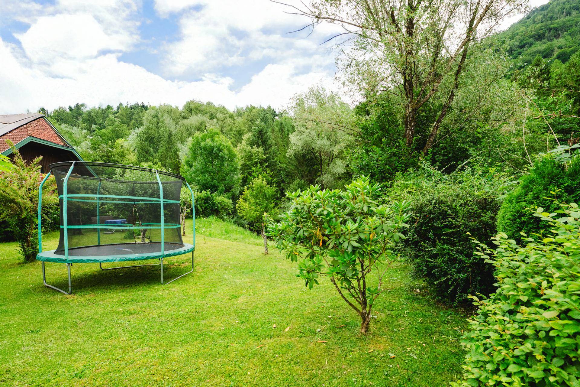 Großer Garten mit einem Trampolin, umgeben von Bäumen und Sträuchern für Freizeitaktivitäten.