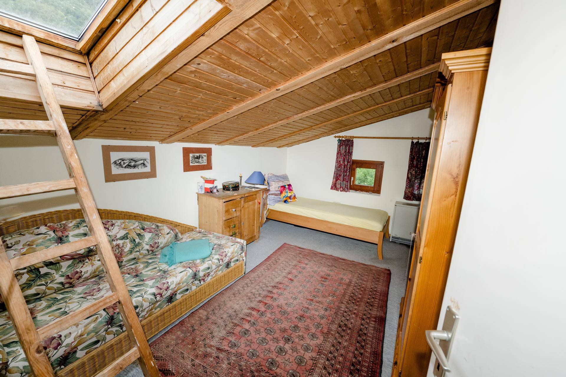Gemütliches Dachgeschoss-Schlafzimmer mit Holzverkleidung, zwei Betten und einem Dachfenster.