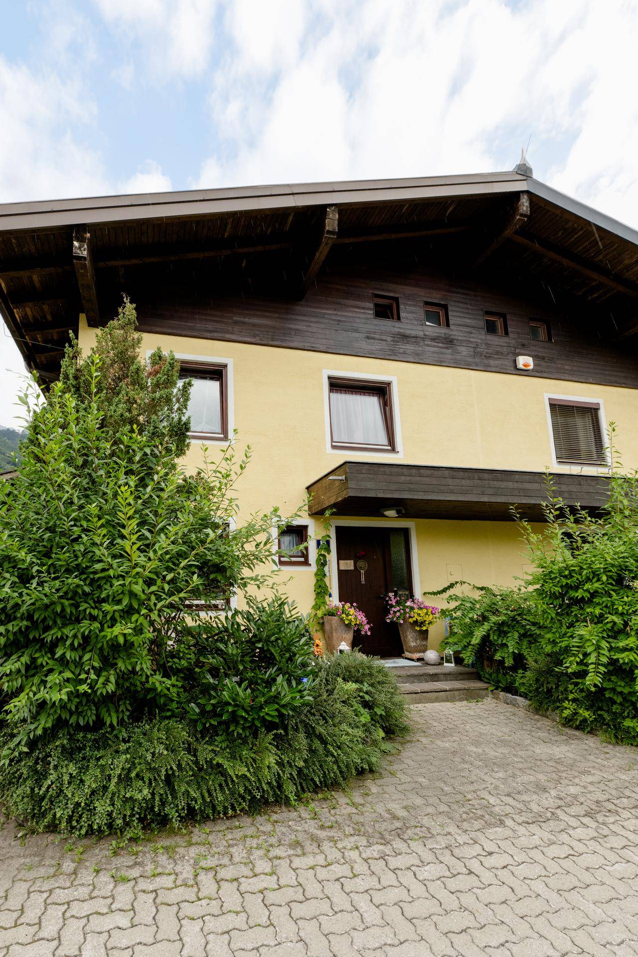 Attraktive Hausfassade mit Eingangsbereich, gelber Farbe und gepflasterter Zufahrt.