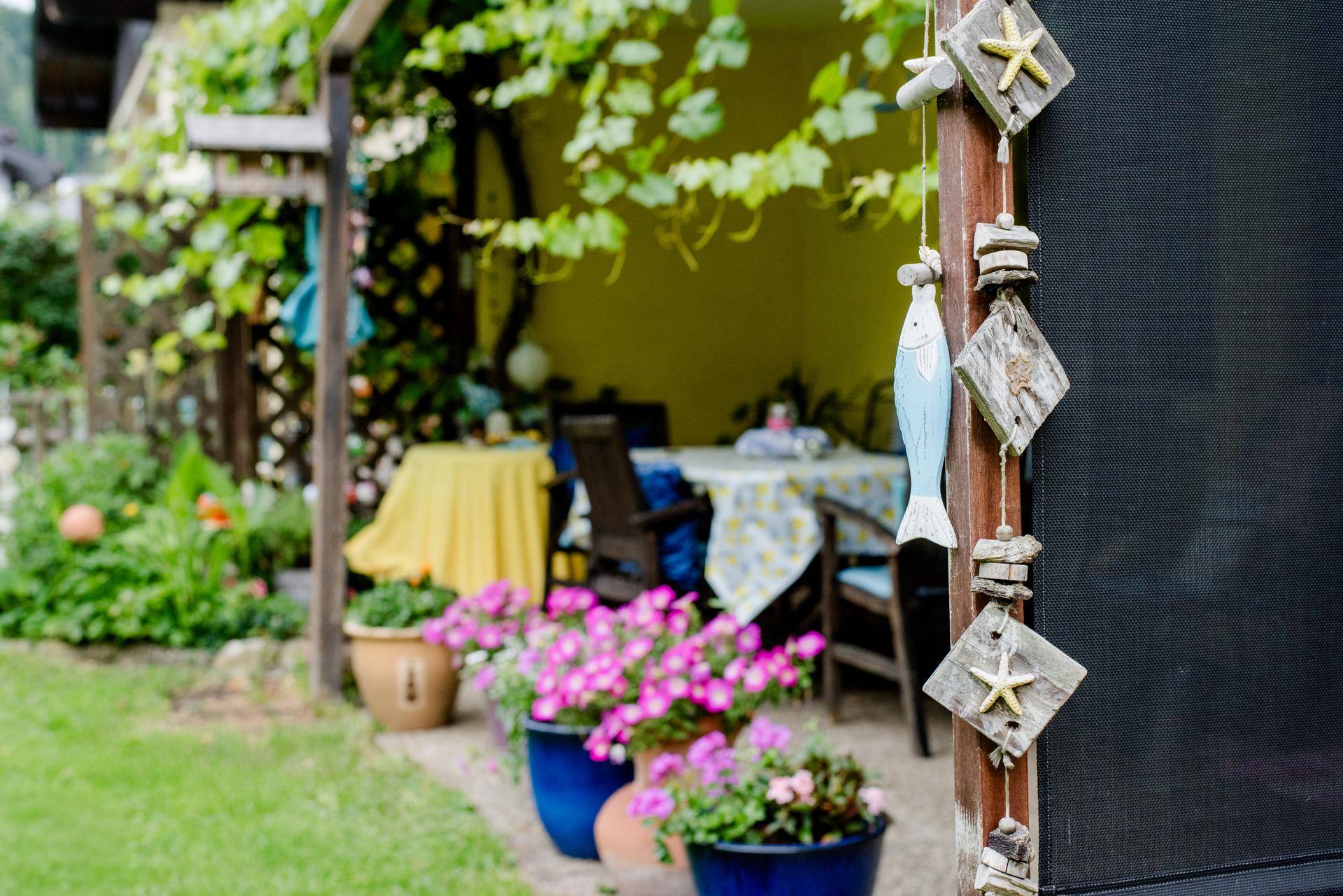 Gemütlicher überdachter Sitzbereich im Freien, dekoriert mit Blumen und maritimen Elementen.
