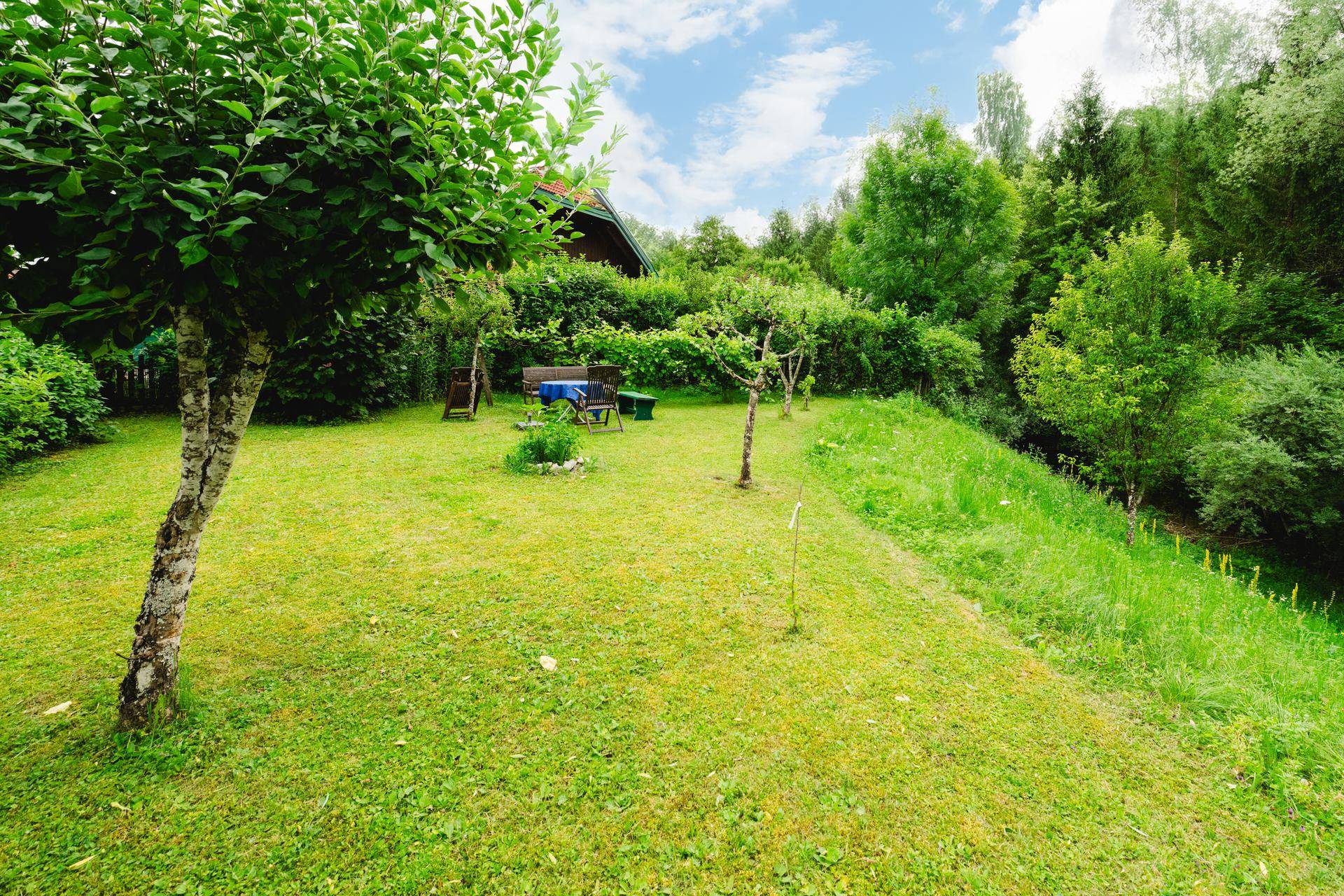 Gepflegter Garten mit Rasenfläche, jungen Obstbäumen und einer kleinen Sitzecke im Hintergrund.