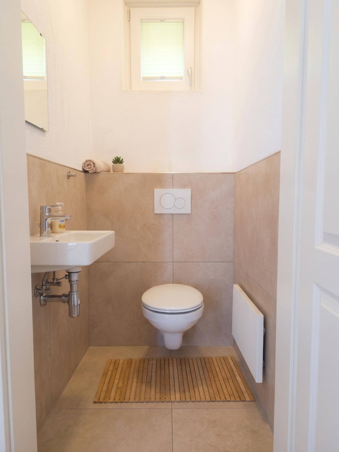 Kleines Gäste-WC mit Wand-WC, Waschbecken und Fenster.