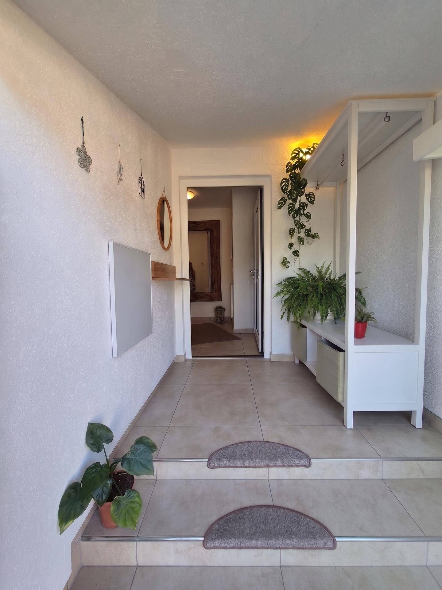 Heller Eingangsbereich mit Fliesenboden, Garderobe und Pflanzen.