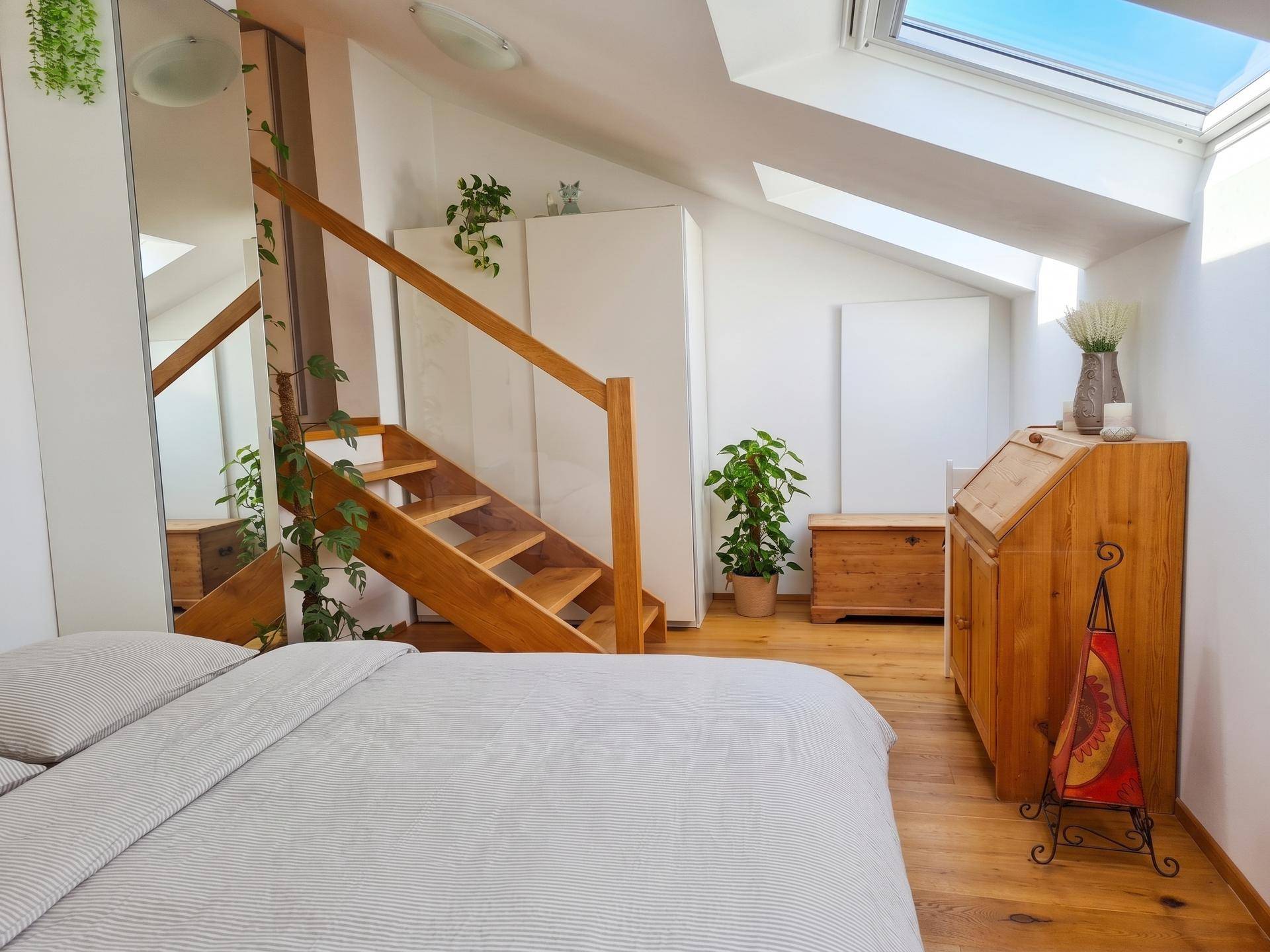 Gemütliches Schlafzimmer im Dachgeschoss mit Holzboden, Dachfenstern und offener Treppe.