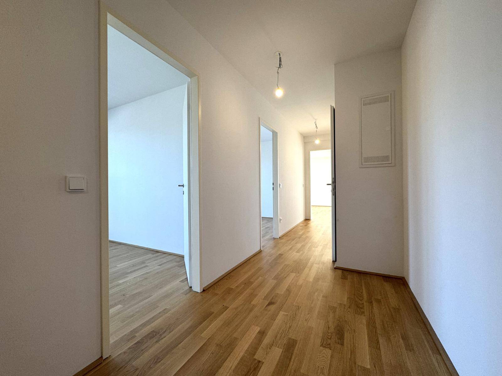 Heller Flur mit Holzboden und weißen Wänden, der zu den verschiedenen Zimmern führt.