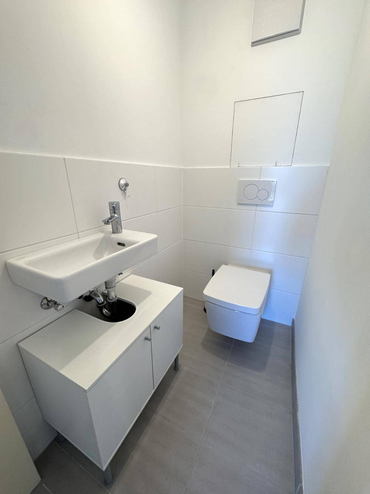 Modernes Gäste-WC mit wandhängendem WC, kleinem Waschbecken und hellen Fliesen.
