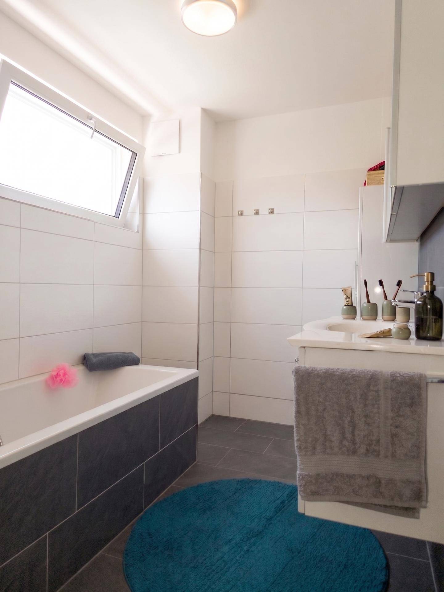 Modernes Badezimmer mit Badewanne, Dusche und Fenster für Tageslicht.