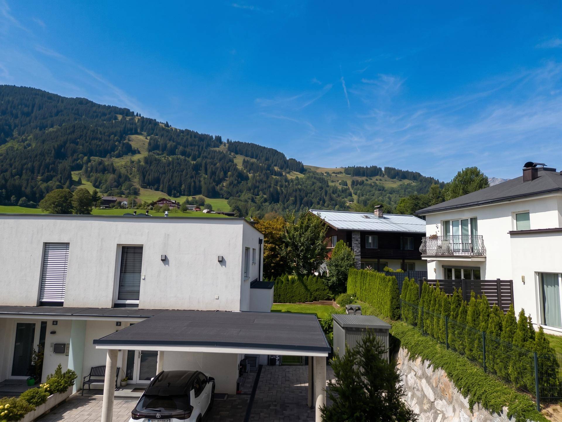 Moderne Häuser in einer grünen Berglandschaft unter blauem Himmel.