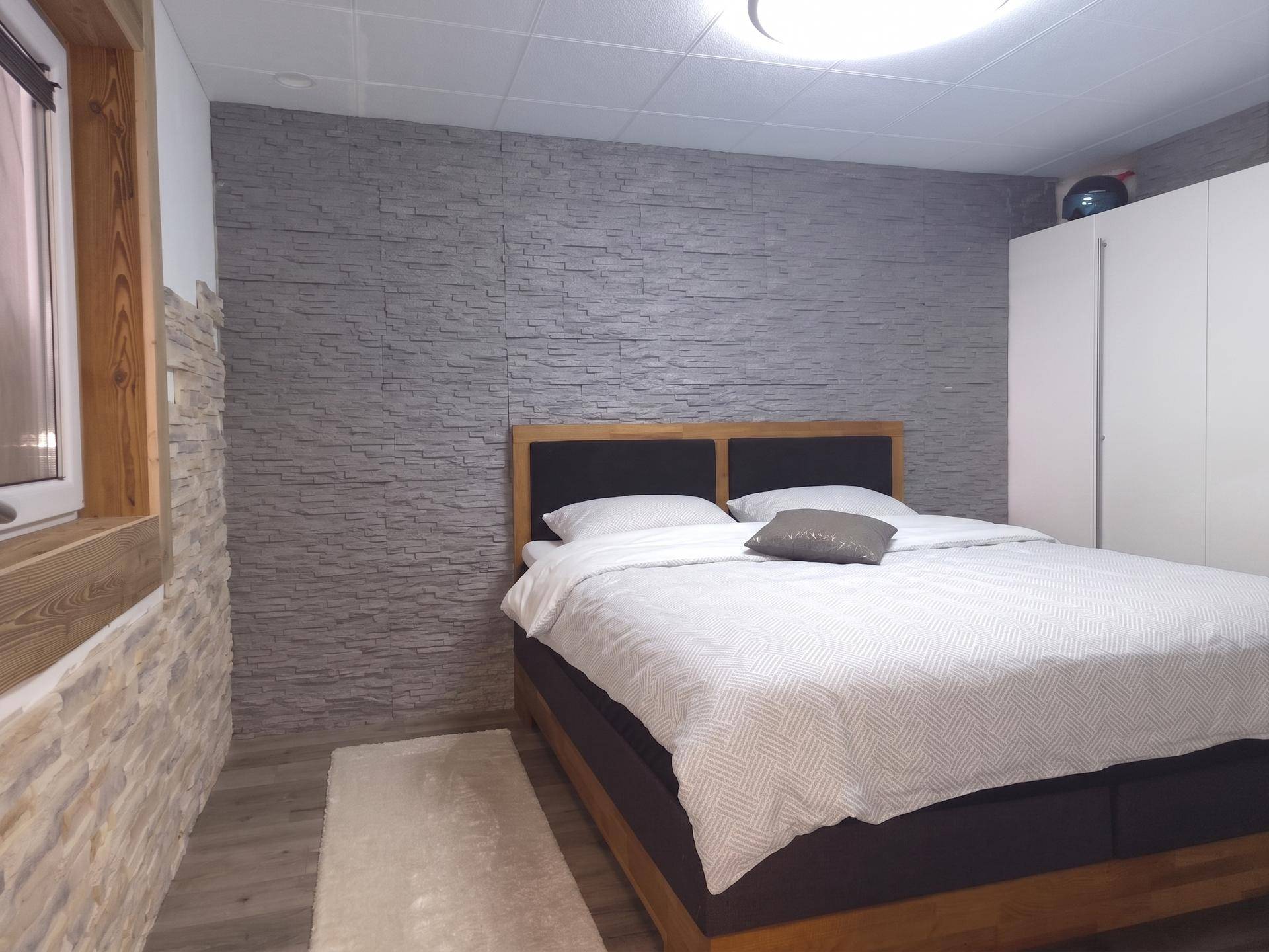 Schlafzimmer mit Doppelbett, Holzboden und dekorativer Steinwand.