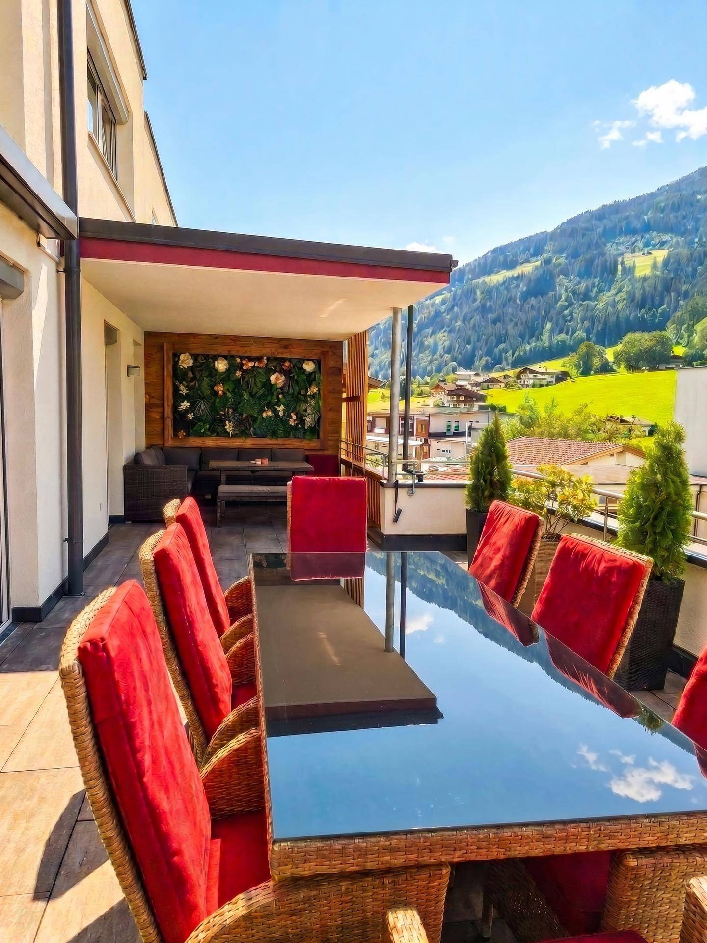 Sonniger Terrassenbereich mit großem Esstisch und Panoramablick auf die Berge.