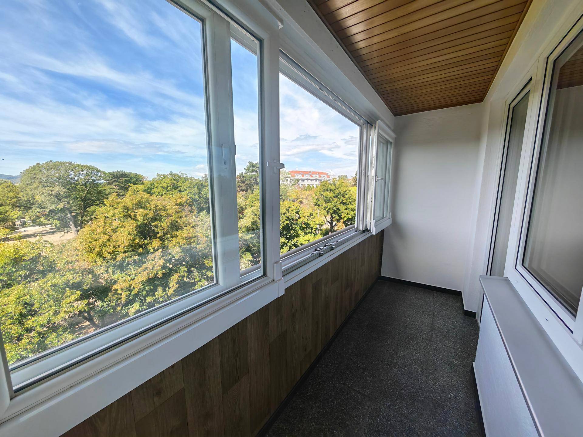 Verglaster Balkon mit Fliesenboden und weitem Blick ins Grüne und auf die Umgebung.