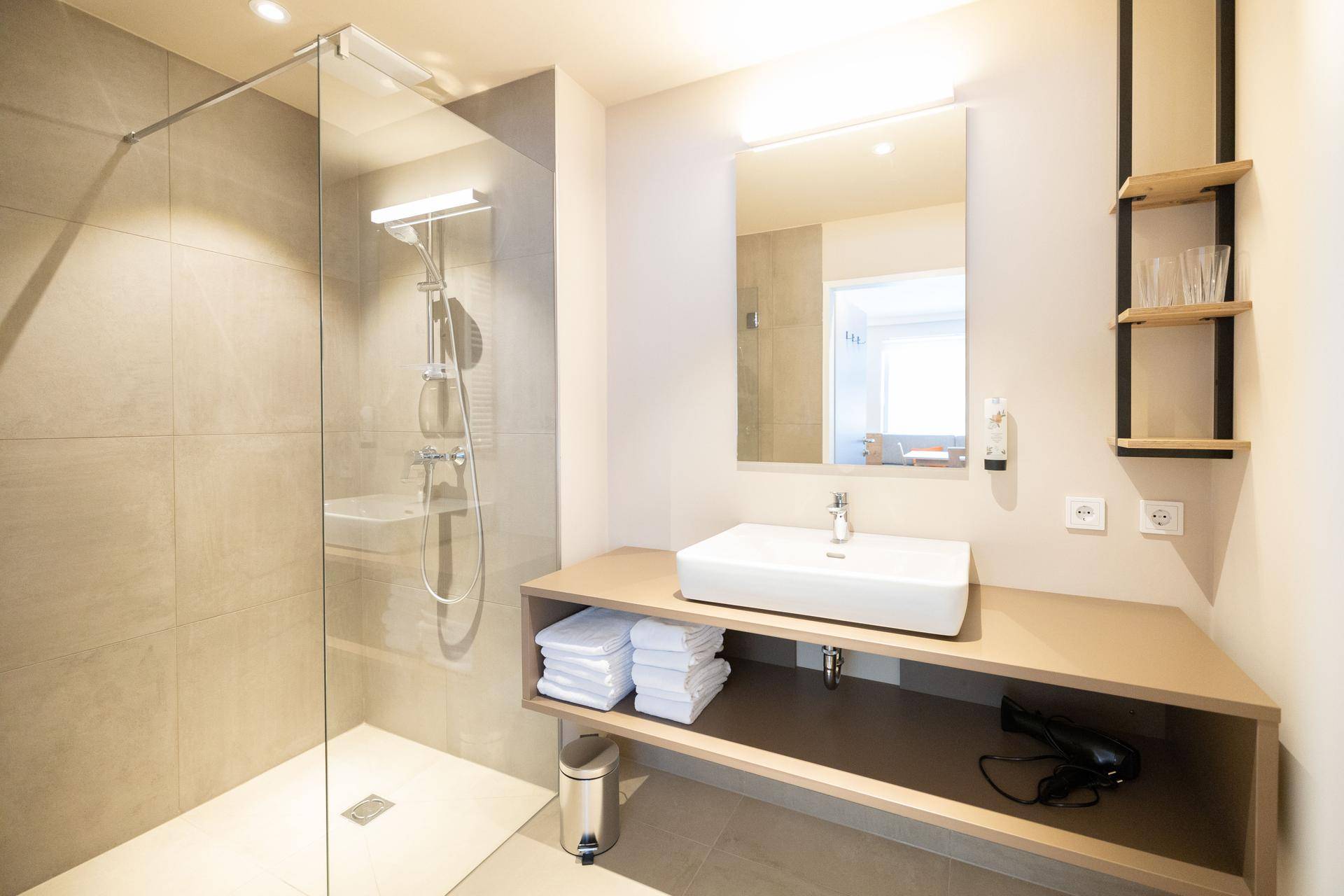 Modernes Badezimmer mit ebenerdiger Dusche, großem Waschbecken und hellen Fliesen.