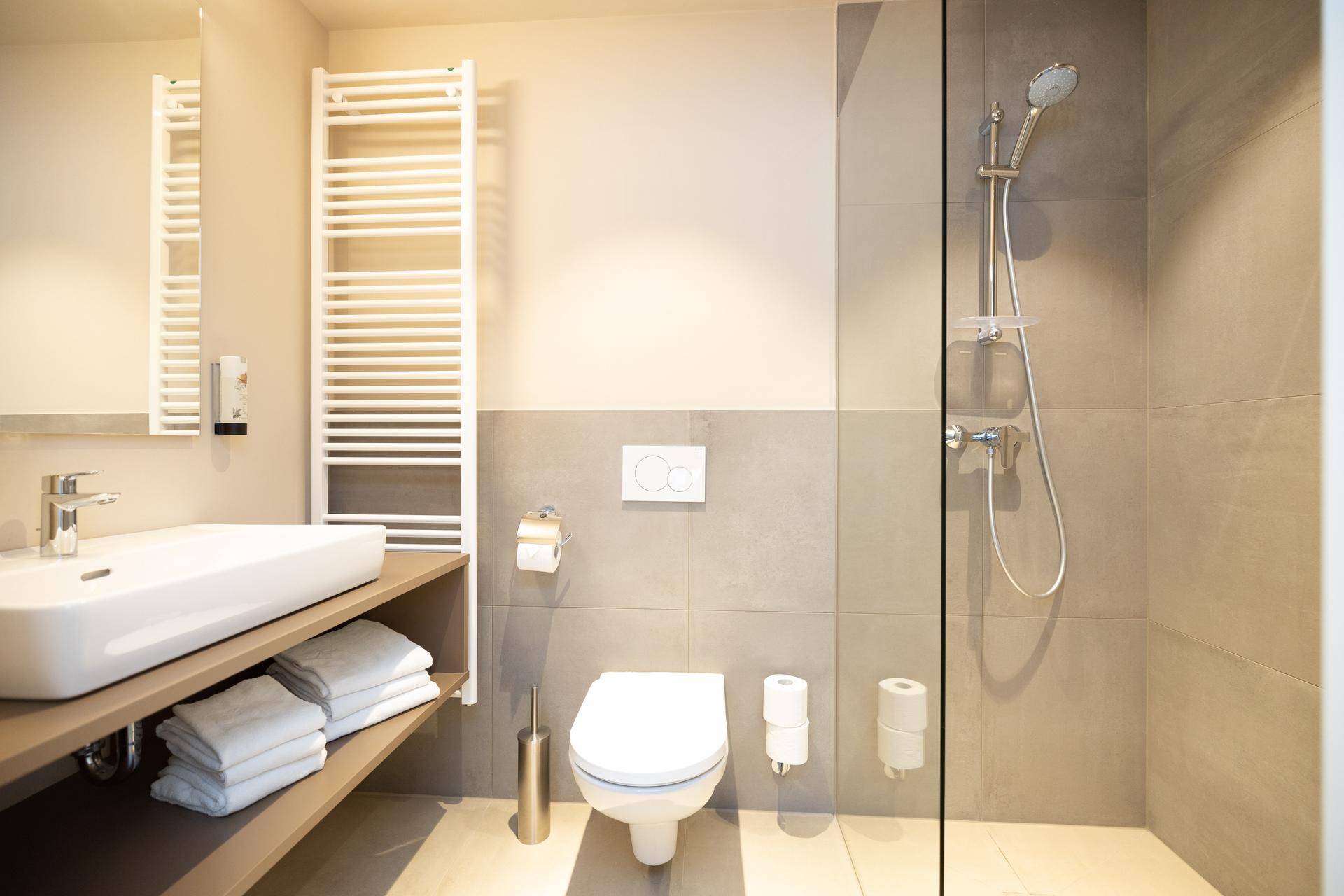 Zeitgemäßes Badezimmer mit ebenerdiger Dusche, WC, Waschbecken und beheiztem Handtuchhalter.