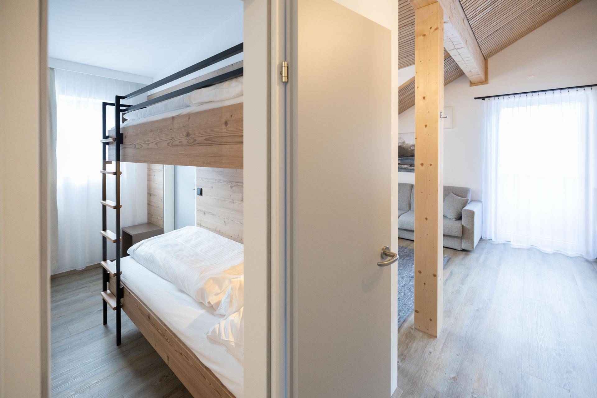 Blick aus dem Schlafzimmer mit Etagenbett in den hellen Wohnbereich mit Dachschräge und Fenster.