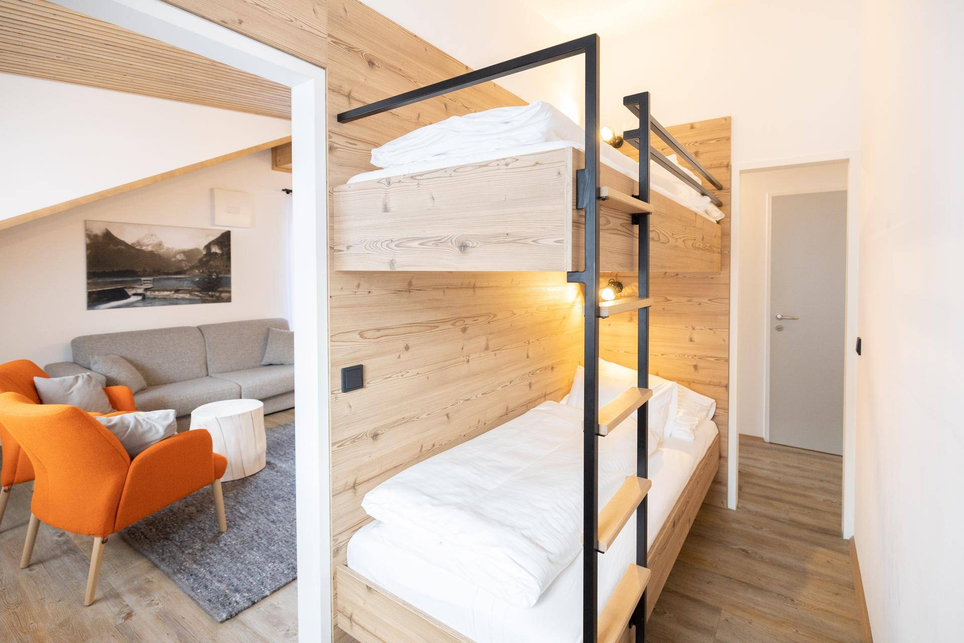 Modernes Schlafzimmer mit Etagenbett und Holzwand, offen zum angrenzenden Wohnbereich.