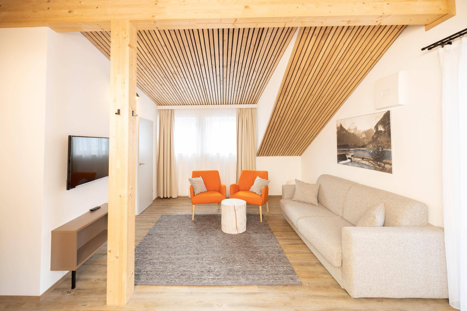 Gemütliches Wohnzimmer mit schrägen Holzdecken, bequemer Couch und zwei orangefarbenen Sesseln.