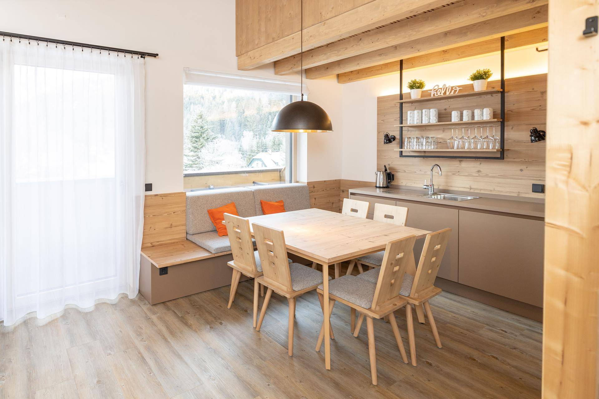 Heller Wohn-Essbereich mit moderner Küchenzeile, Holztisch und gemütlicher Sitzecke am Fenster.