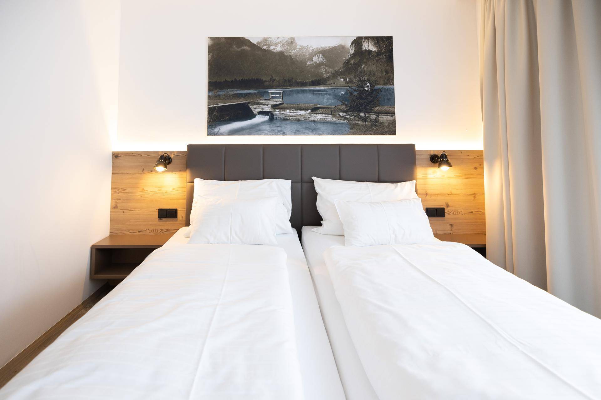Helles Schlafzimmer mit zwei Einzelbetten, Holzkopfteil und Wandkunst.