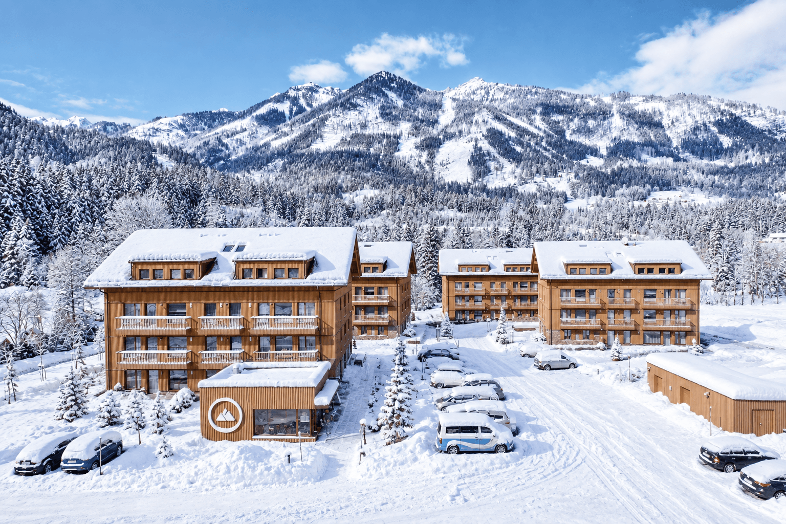 Gesamtanlage des Aparthotels mit mehreren modernen Holzgebäuden in einer weitläufigen, verschneiten Berglandschaft.