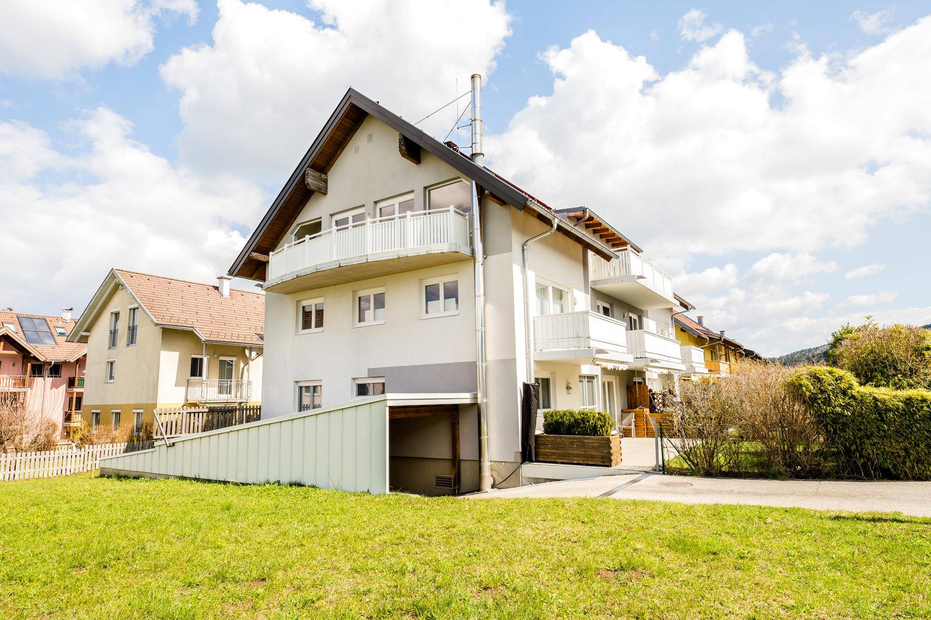 Modernes Mehrfamilienhaus mit mehreren Balkonen, Satteldach und Zufahrt zur Tiefgarage.