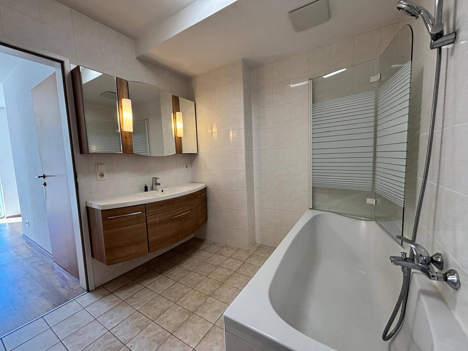 Modernes Badezimmer mit Badewanne, Einzelwaschbecken und hellen Fliesen an Wänden und Boden.