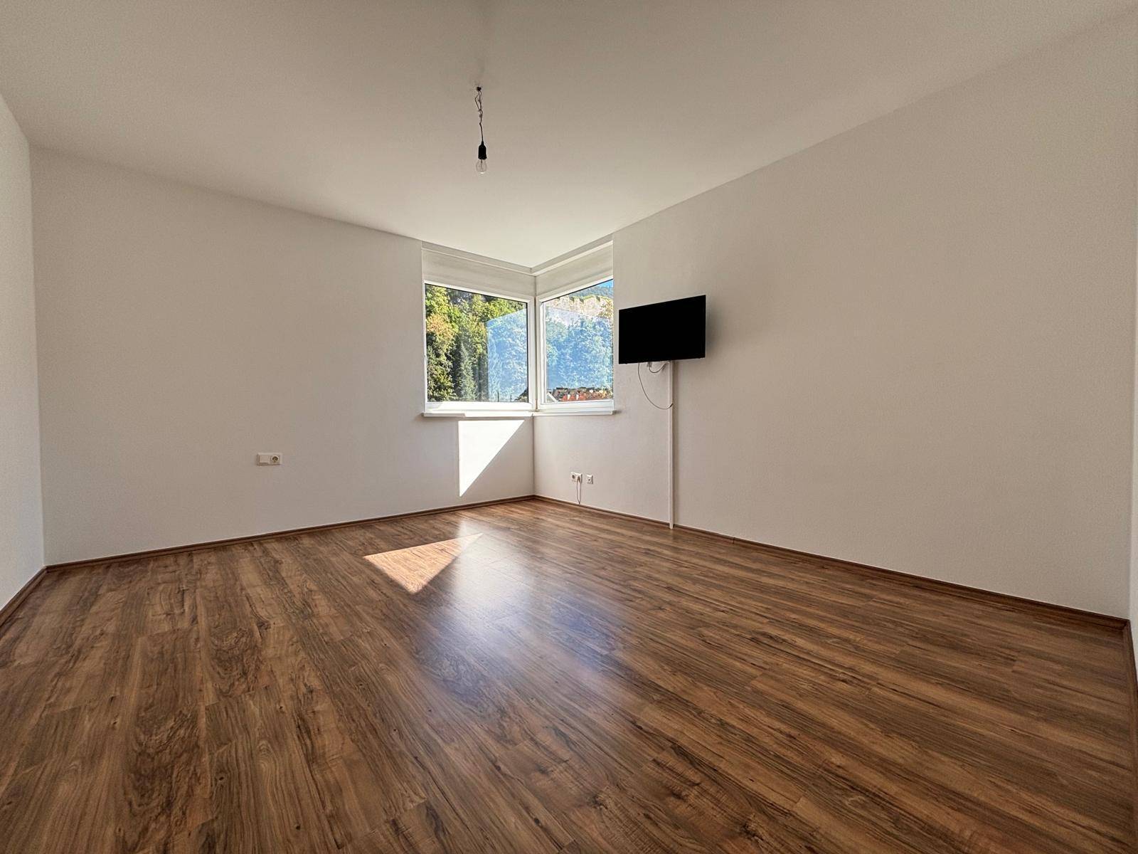Geräumiges Zimmer mit Laminatboden und Eckfenstern, die viel Tageslicht hereinlassen.
