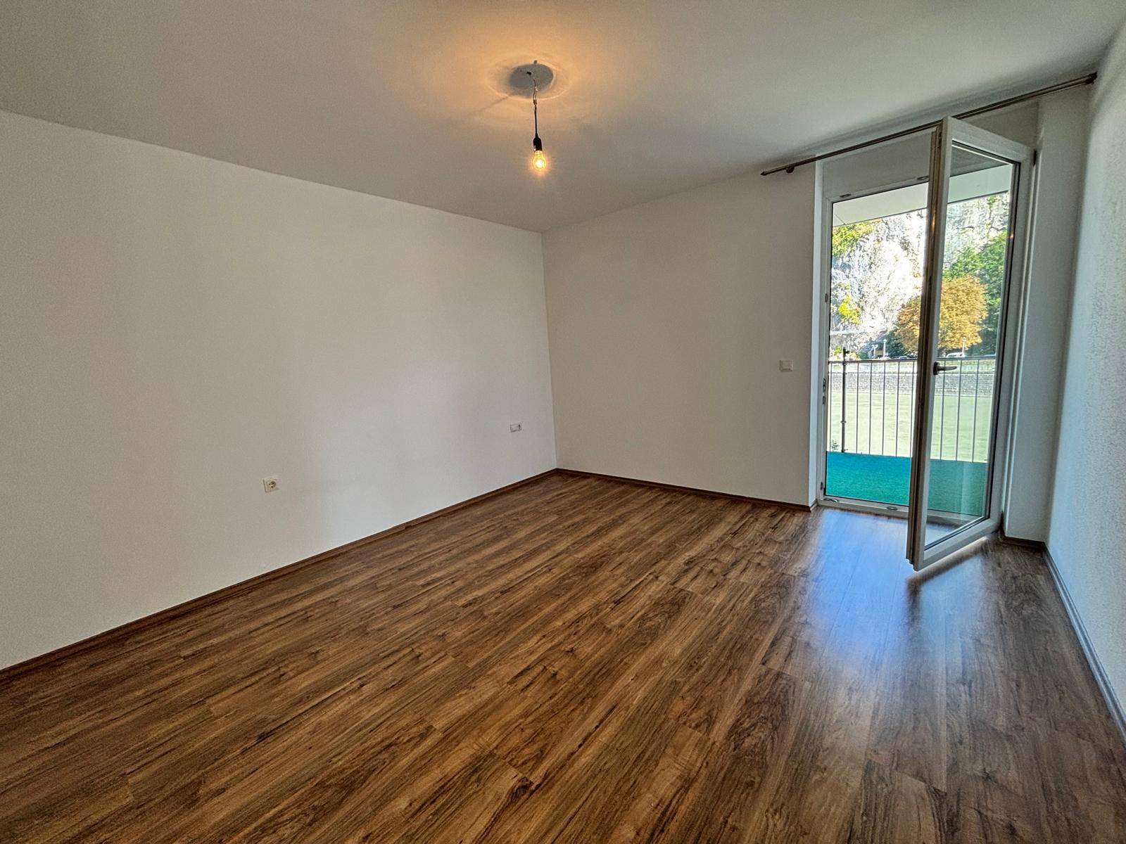 Geräumiges Zimmer mit Laminatboden und einer Tür, die zu einem sonnigen Außenbereich führt.