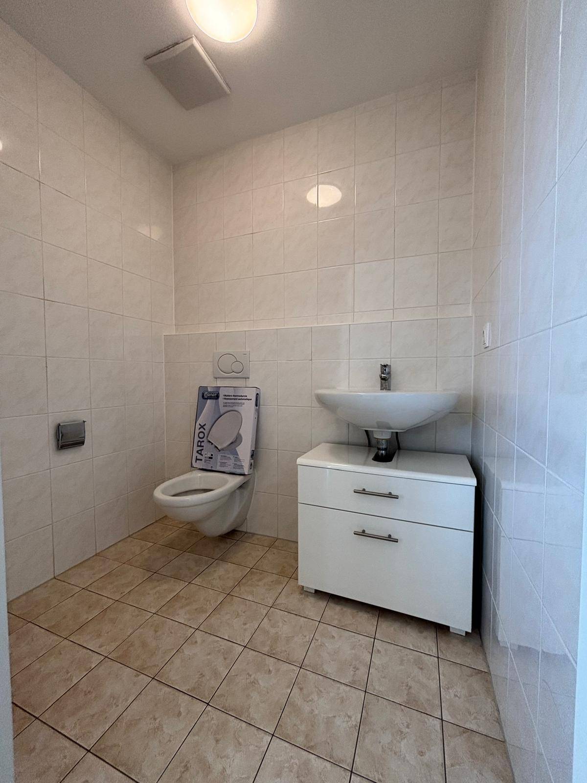 Funktionale Gästetoilette mit WC, kleinem Waschbecken und hellen Fliesen an Wänden und Boden.