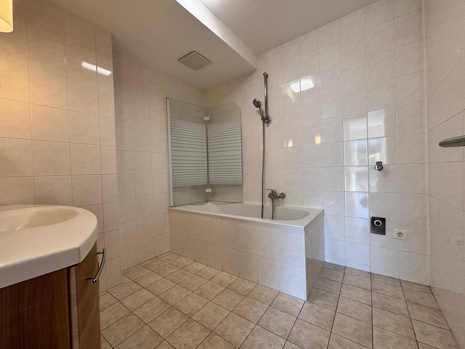 Helles Badezimmer mit Badewanne, Duschvorrichtung und vollständig gefliesten Wänden und Boden.