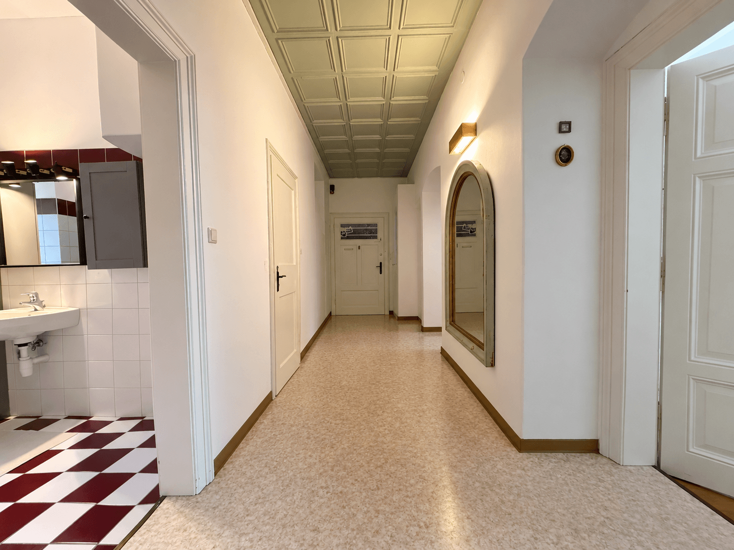 Langer Flur mit Terrazzoboden, dekorativer Decke und Zugang zu einem Badezimmer.