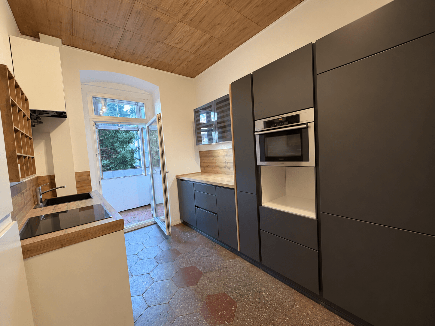 Moderne Küche mit dunklen Schränken, Holzarbeitsplatten und Zugang zu einem kleinen Balkon.