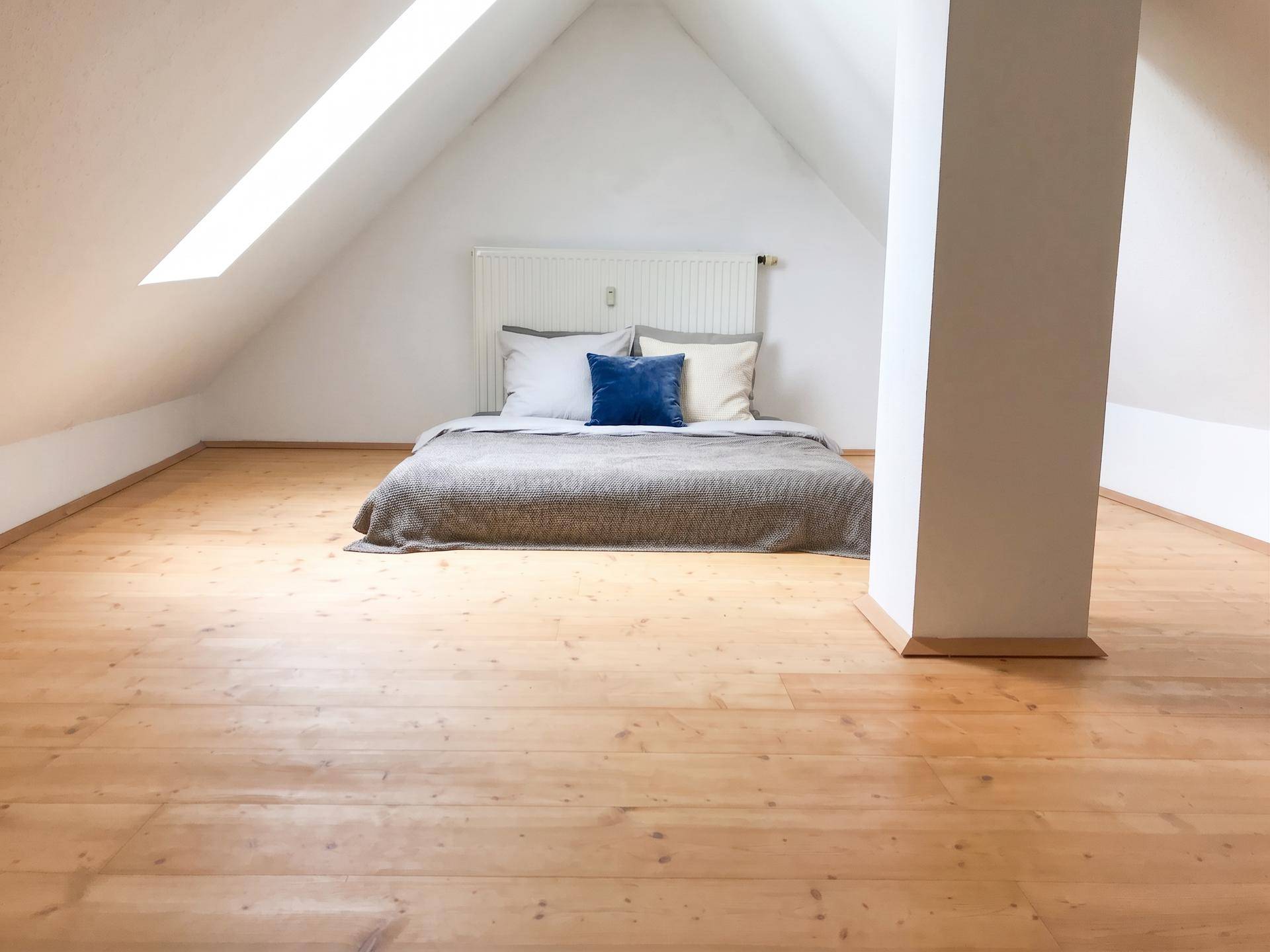 Helles Schlafzimmer im Dachgeschoss mit Holzdielenboden, Dachschrägen und einem großen Dachfenster.