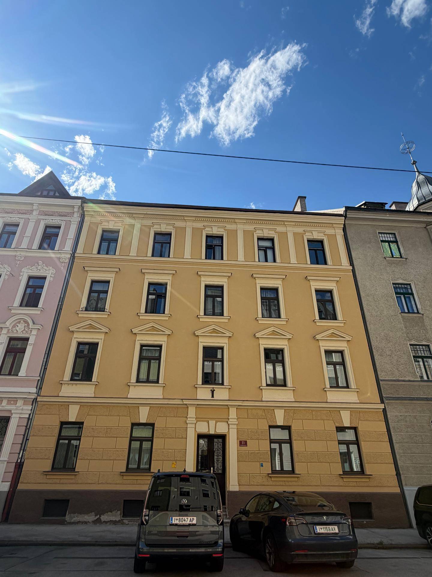 Historisches Wohngebäude mit gelber Fassade und vielen Fenstern unter blauem Himmel.