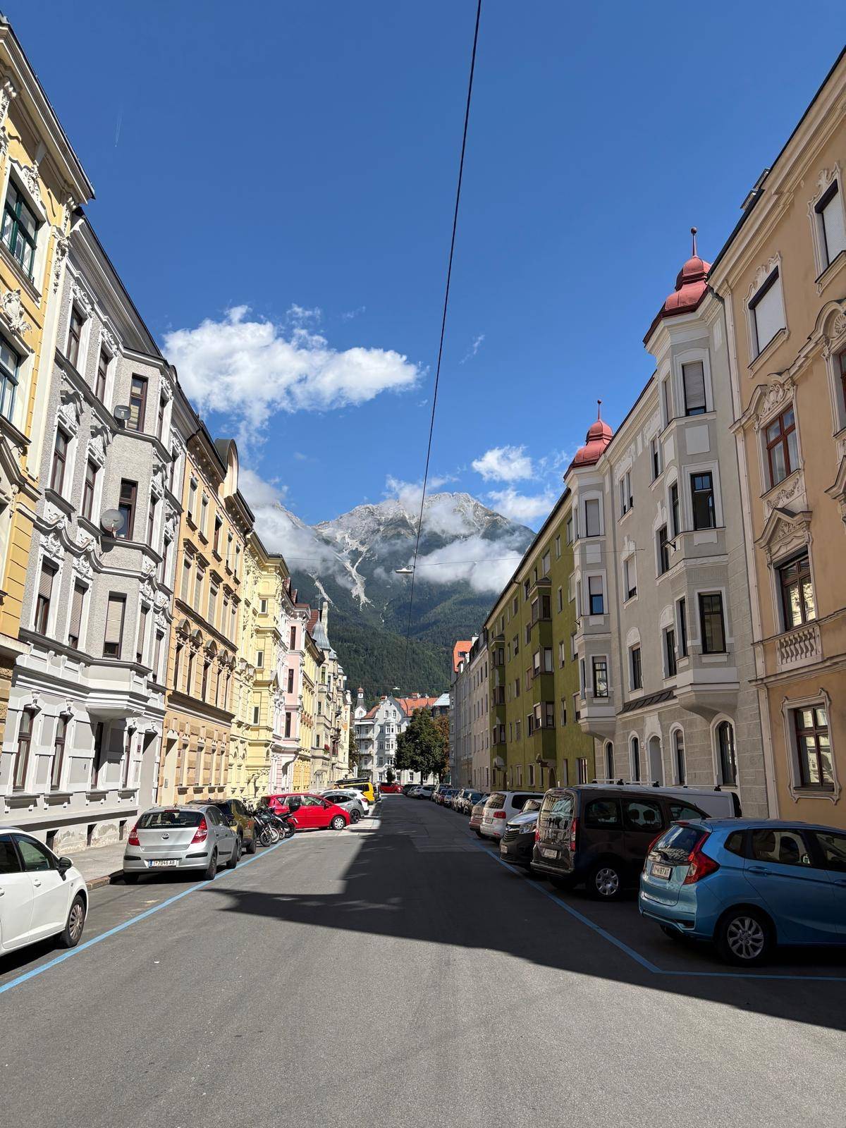 Malerische Straße mit bunten Gebäuden und beeindruckendem Bergblick im Hintergrund.
