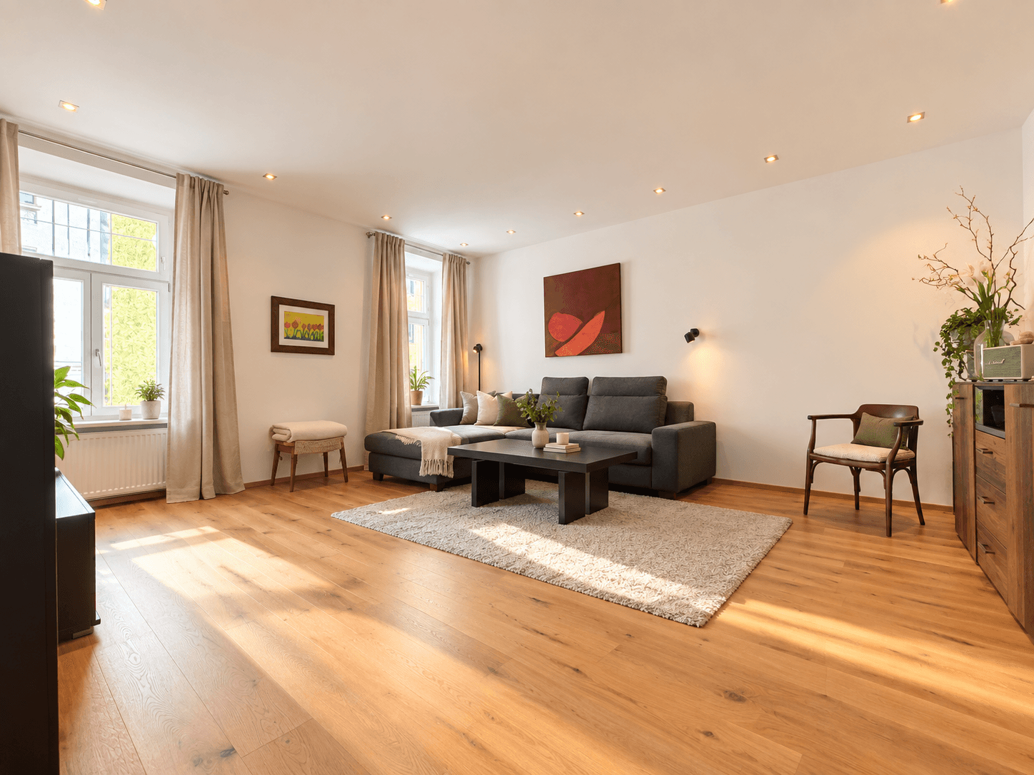 Lichtdurchflutetes Wohnzimmer mit Holzboden, großen Fenstern und gemütlicher Sitzecke.