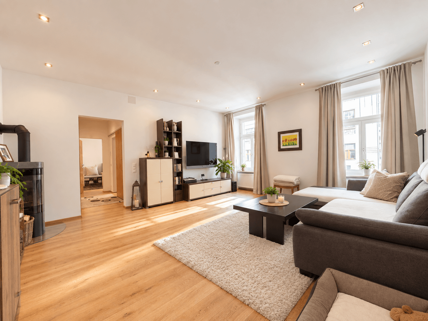 Geräumiges Wohnzimmer mit Holzboden, großem Sofa und einem modernen Kaminofen.