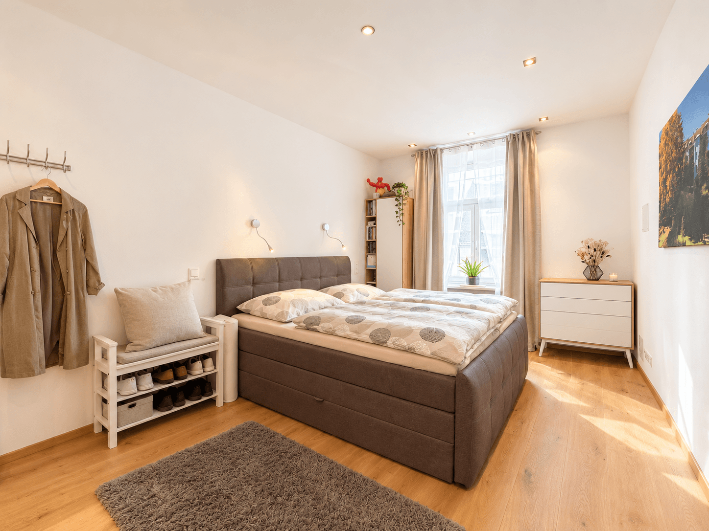 Helles Schlafzimmer mit Doppelbett, Holzboden und einem Fenster mit Vorhängen.