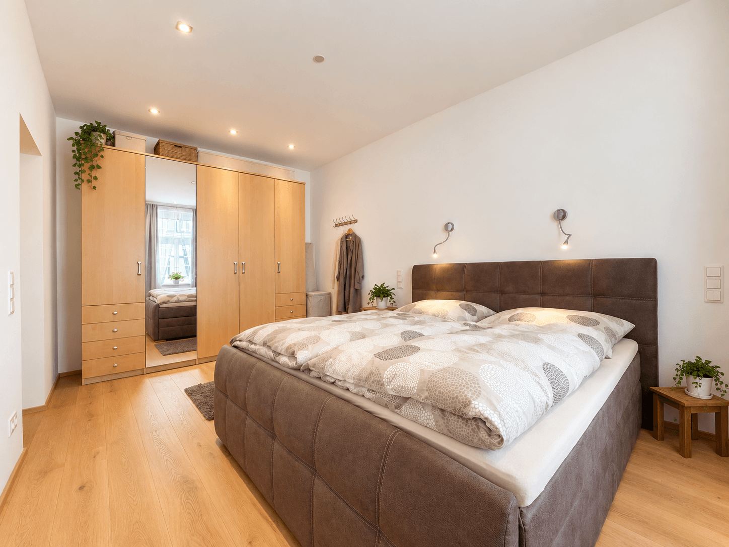 Schlafzimmer mit großem Doppelbett, Holzboden und Einbauschränken mit Spiegelfronten.